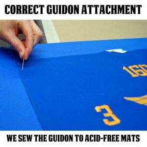 Sewing a guidon to an acid-free mat is a correct way to attach the guidon inside the frame